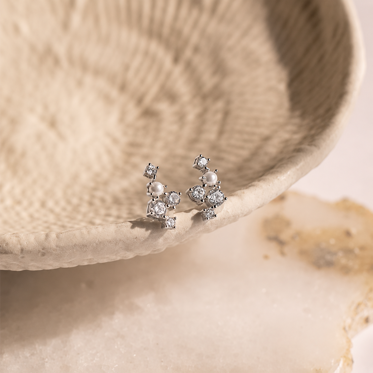 Silver earrings with pearls and crystals on a beige shell